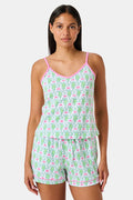 A woman wearing the SERFLEX Monkey Mischa Set, a coordinated sleeveless top and shorts with pink straps and a fun pink and green flamingo print, made from soft Pima cotton, stands against a plain white background.