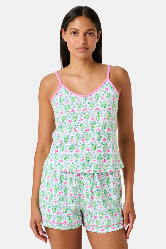 A woman wearing the SERFLEX Monkey Mischa Set, a coordinated sleeveless top and shorts with pink straps and a fun pink and green flamingo print, made from soft Pima cotton, stands against a plain white background.