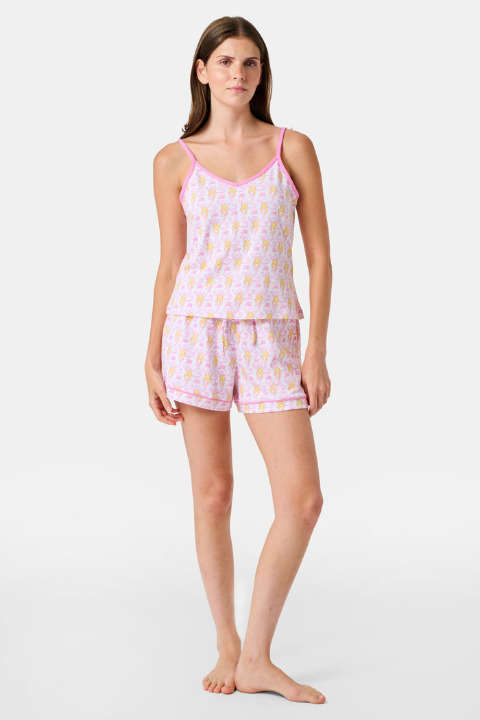 A woman wearing the Roller Rabbit Monkey Mischa Set stands with one hand in her pocket against a plain white background. This pajama set features a light pink flamingo print camisole and matching shorts, crafted from soft Pima cotton for comfort and style in women’s sleepwear.