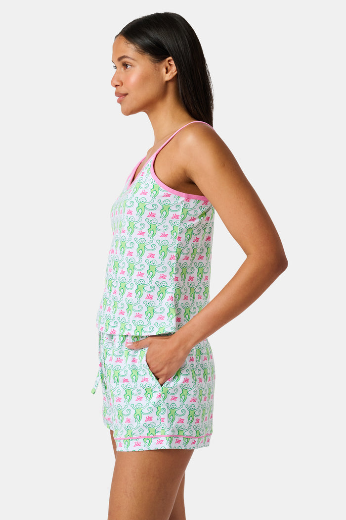 A woman wearing the SERFLEX Monkey Mischa Set, a coordinated sleeveless top and shorts with pink straps and a fun pink and green flamingo print, made from soft Pima cotton, stands against a plain white background.