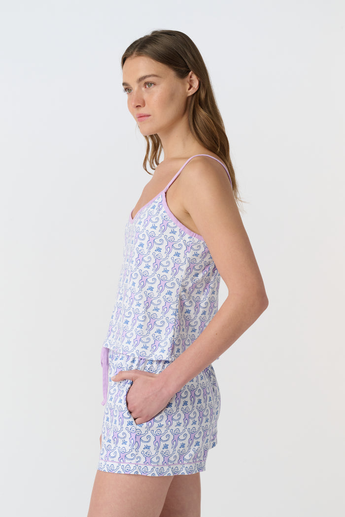 A woman smiles while wearing the Roller Rabbit Monkey Mischa Set—a sleeveless, light purple and white patterned romper with pockets and a drawstring waist—standing against a plain white background.