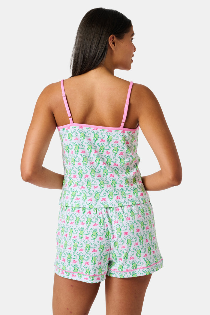A woman wearing the SERFLEX Monkey Mischa Set, a coordinated sleeveless top and shorts with pink straps and a fun pink and green flamingo print, made from soft Pima cotton, stands against a plain white background.