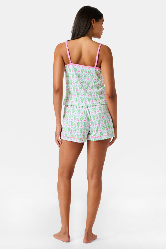 A woman wearing the SERFLEX Monkey Mischa Set, a coordinated sleeveless top and shorts with pink straps and a fun pink and green flamingo print, made from soft Pima cotton, stands against a plain white background.
