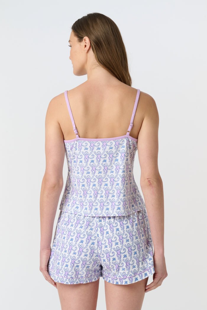 A woman smiles while wearing the Roller Rabbit Monkey Mischa Set—a sleeveless, light purple and white patterned romper with pockets and a drawstring waist—standing against a plain white background.