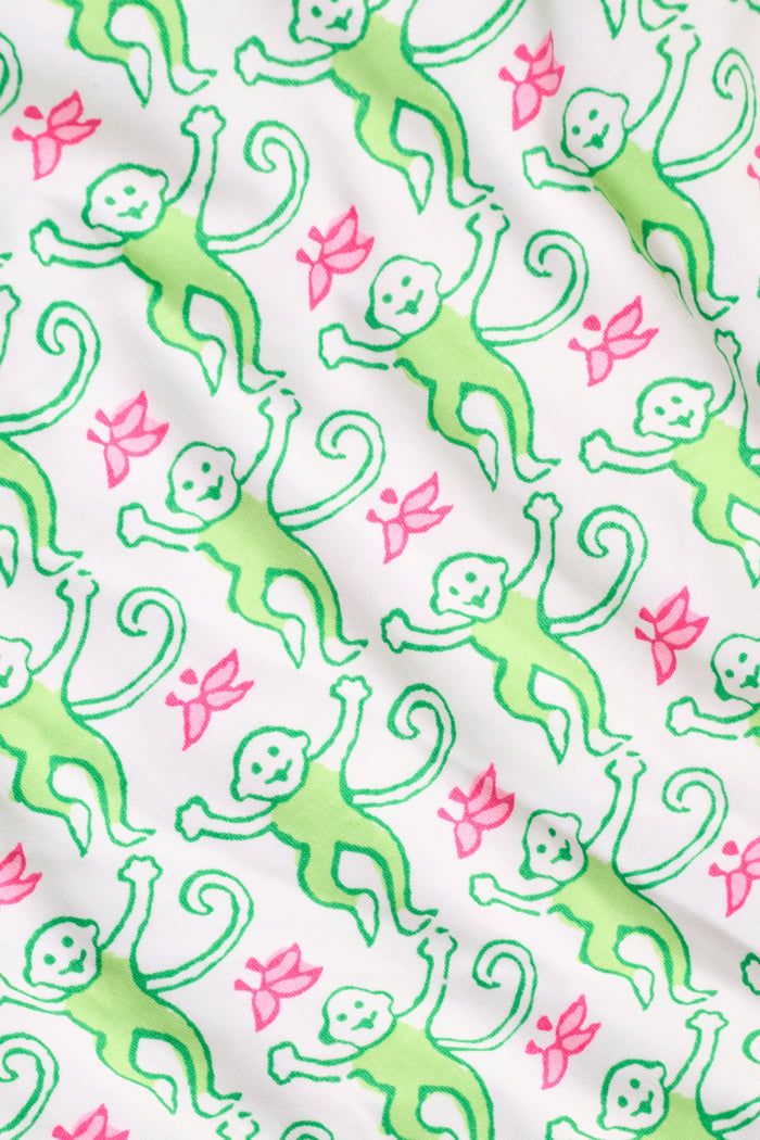 A woman wearing the Roller Rabbit Monkey Polo Pajamas, a short-sleeve button-up set with matching shorts featuring a green and pink floral pattern, stands against a plain white background.
