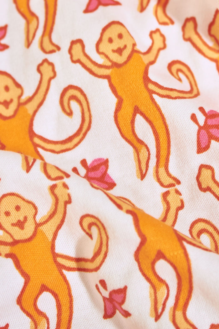 A woman wears the Roller Rabbit Monkey Mischa Set, a white Pima cotton pajama with an orange and pink monkey print, featuring a sleeveless top with pink straps and matching shorts with a pink drawstring, standing against a plain white background.