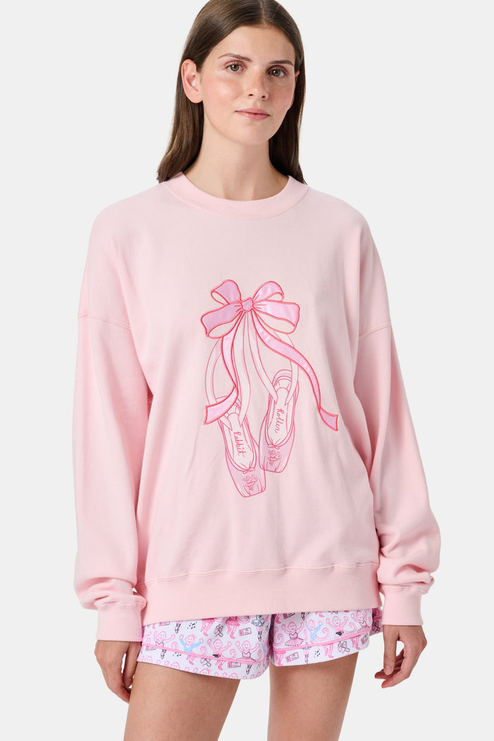 A person with long blonde hair in a ballet slipper-pink Roller Rabbit Monkey Pirouette Andie Sweatshirt holds patterned folders in front of white lockers.