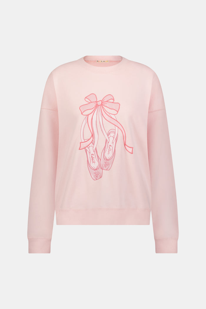 A person with long blonde hair in a ballet slipper-pink Roller Rabbit Monkey Pirouette Andie Sweatshirt holds patterned folders in front of white lockers.