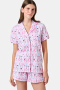 The Monkey Pirouette Polo Pajamas by Roller Rabbit feature a pink short-sleeve button-up top and matching shorts, adorned with a colorful and playful monkey, animal, and floral pattern on a white background.