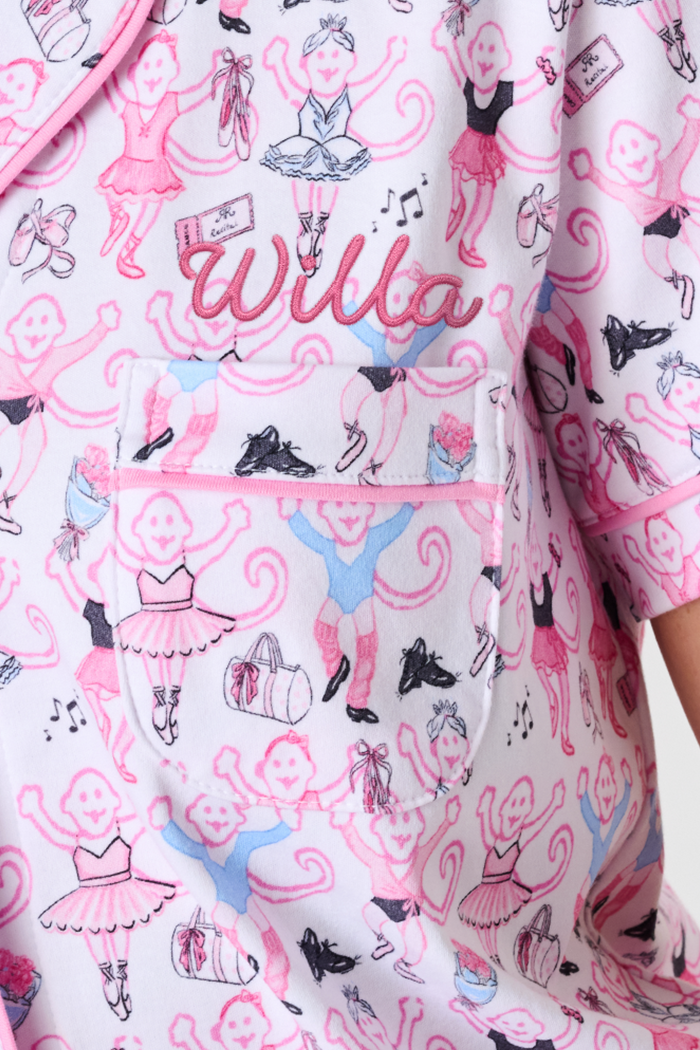 The Monkey Pirouette Polo Pajamas by Roller Rabbit feature a pink short-sleeve button-up top and matching shorts, adorned with a colorful and playful monkey, animal, and floral pattern on a white background.