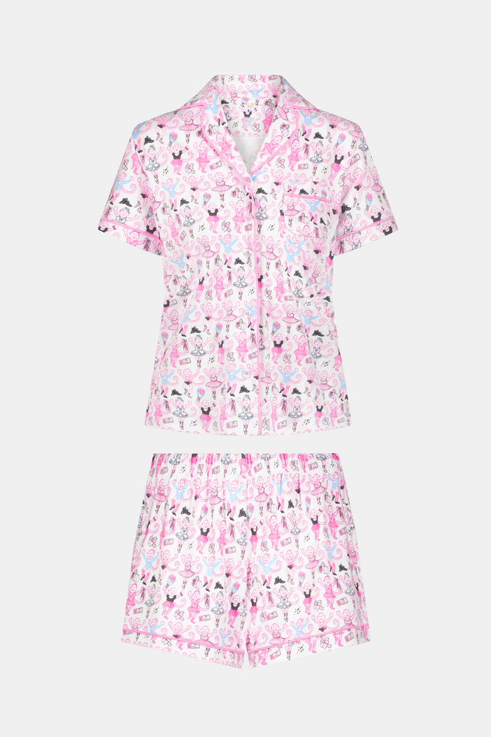 The Monkey Pirouette Polo Pajamas by Roller Rabbit feature a pink short-sleeve button-up top and matching shorts, adorned with a colorful and playful monkey, animal, and floral pattern on a white background.