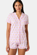 Introducing the Monkey Fiora Pajamas from Roller Rabbit—crafted from fabric adorned with a delightful pattern of pink and yellow monkeys with curled tails and smiling faces, interspersed with tiny leaves on a crisp white background. Perfect for adding playful charm to your sleepwear collection.