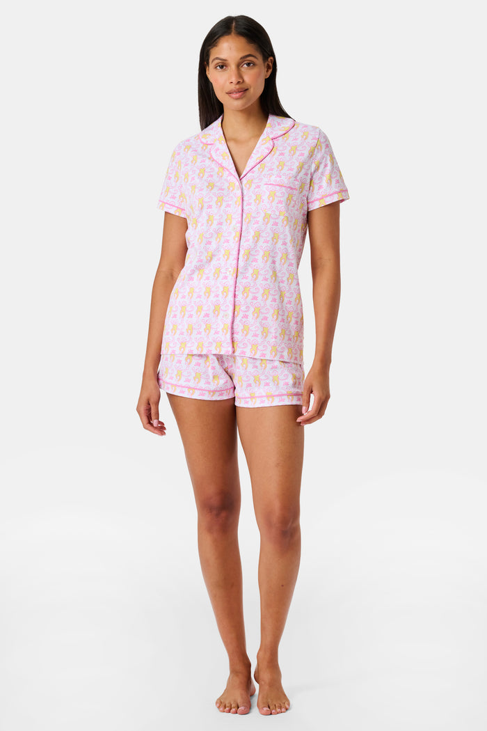 Introducing the Monkey Fiora Pajamas from Roller Rabbit—crafted from fabric adorned with a delightful pattern of pink and yellow monkeys with curled tails and smiling faces, interspersed with tiny leaves on a crisp white background. Perfect for adding playful charm to your sleepwear collection.
