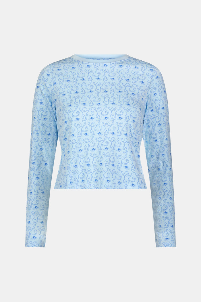 A woman with long brown hair wears the Roller Rabbit Monkey Rosebud Long Sleeve Baby Tee in light blue, featuring a subtle print, and matching shorts, while standing against a plain white background.