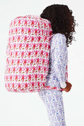 Wearing white and blue pajamas, a person carries the Roller Rabbit Monkey Sleepover Bag—an oversized bag featuring playful monkey prints—on their back. The bag is nearly as large as the person.