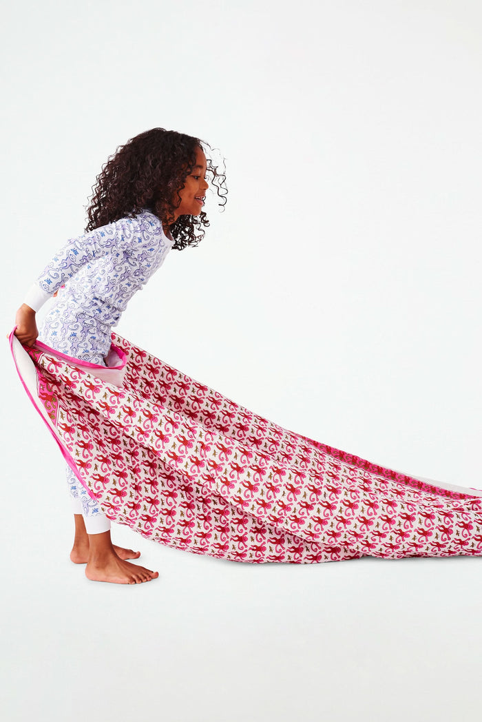 Wearing white and blue pajamas, a person carries the Roller Rabbit Monkey Sleepover Bag—an oversized bag featuring playful monkey prints—on their back. The bag is nearly as large as the person.