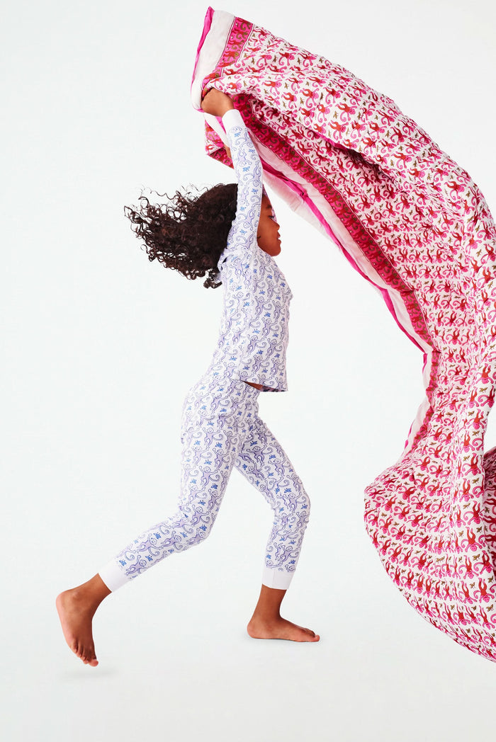 Wearing white and blue pajamas, a person carries the Roller Rabbit Monkey Sleepover Bag—an oversized bag featuring playful monkey prints—on their back. The bag is nearly as large as the person.