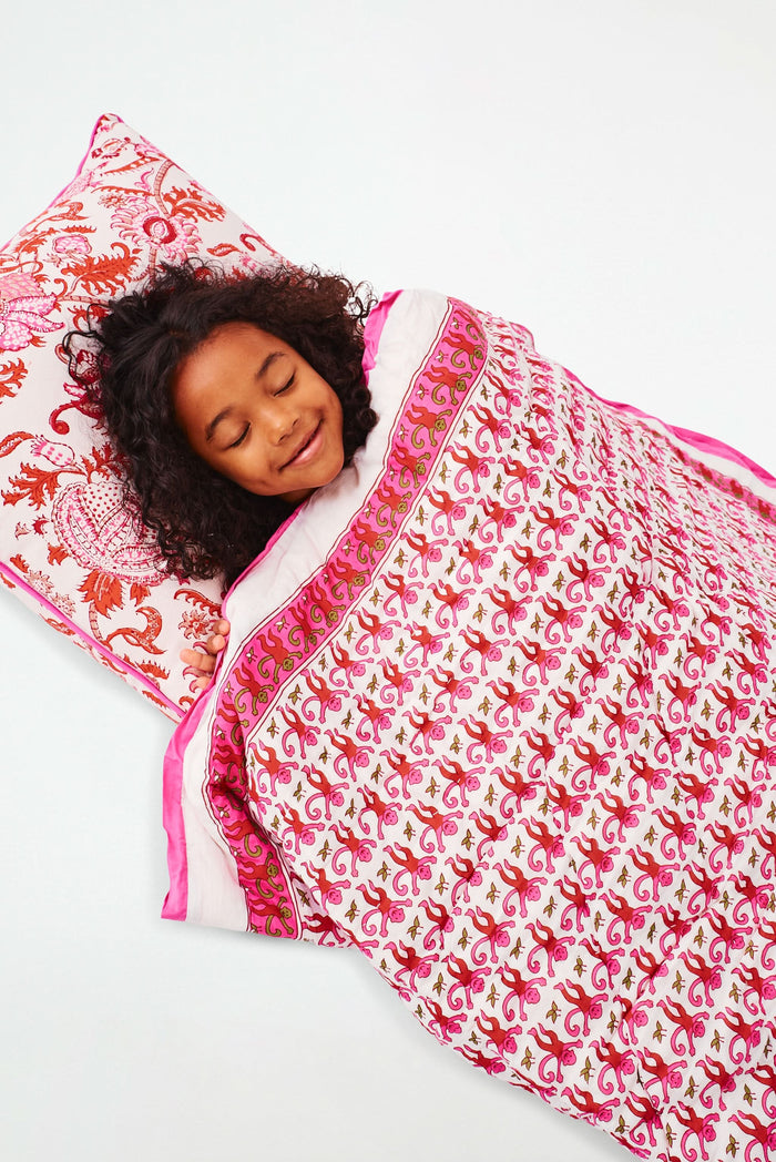 Wearing white and blue pajamas, a person carries the Roller Rabbit Monkey Sleepover Bag—an oversized bag featuring playful monkey prints—on their back. The bag is nearly as large as the person.