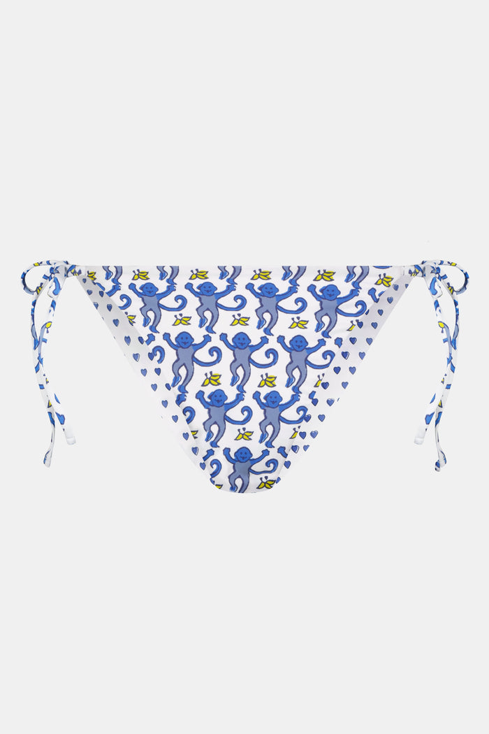 A person is shown from waist to mid-thigh wearing Roller Rabbit's Monkey/Hearts Serena Bikini Bottom, featuring blue heart motifs and blue-and-white side ties. The UPF 50+ swimwear combines stylish design with sun protection.