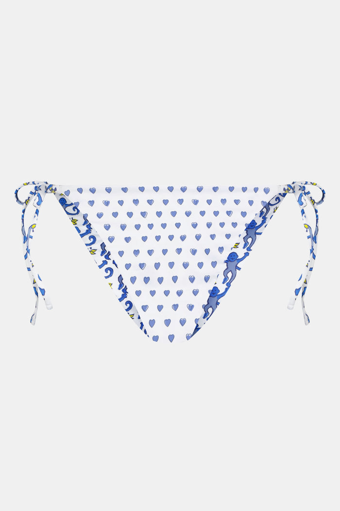 A person is shown from waist to mid-thigh wearing Roller Rabbit's Monkey/Hearts Serena Bikini Bottom, featuring blue heart motifs and blue-and-white side ties. The UPF 50+ swimwear combines stylish design with sun protection.