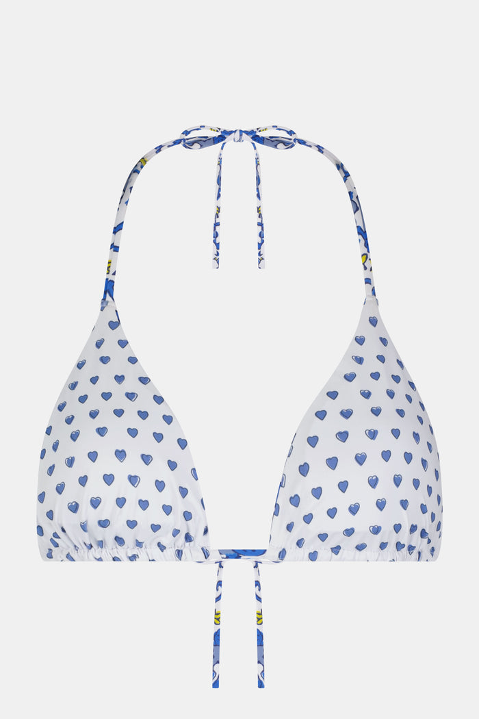 A woman wearing the Roller Rabbit Monkey/Hearts Serena Bikini Top, a white halter-style swim top with blue hearts, stands against a plain background and smiles softly.