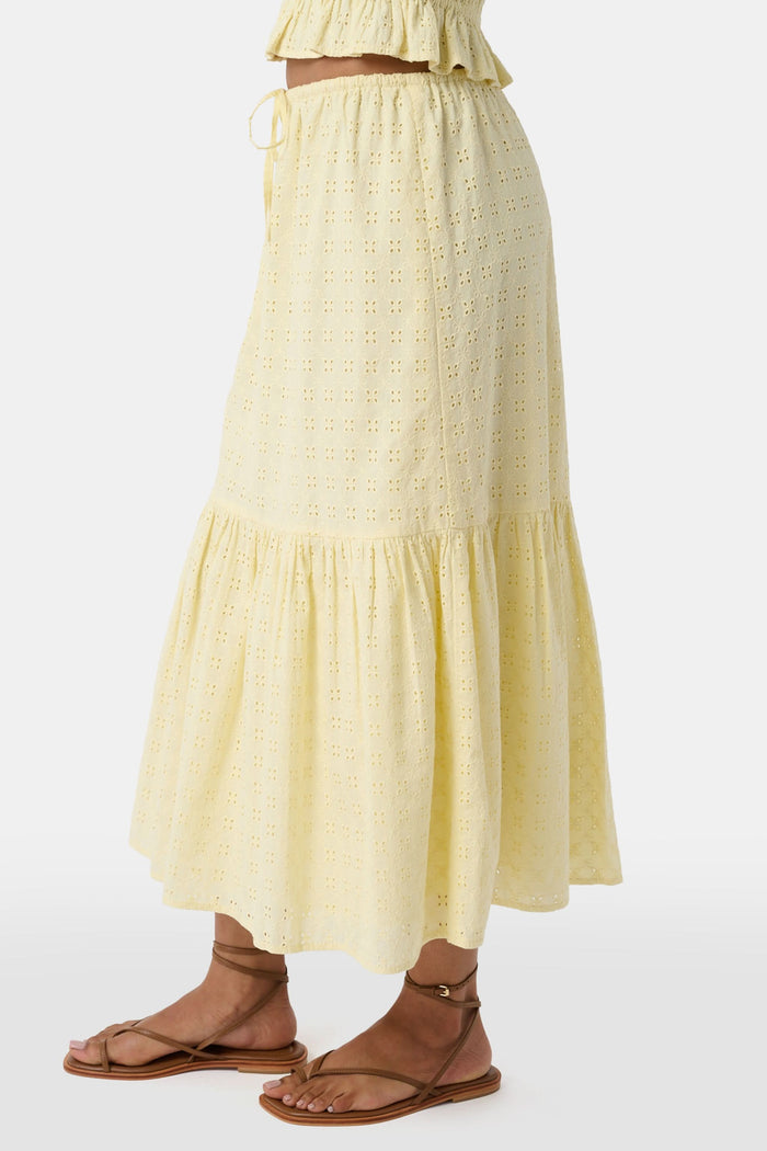 A person wears the Roller Rabbit Petal Eyelet Goldie Skirt, a butter yellow midi with eyelet details, ruffled hem, and gathered top, paired with strappy brown sandals. Their hands rest relaxed by their sides.