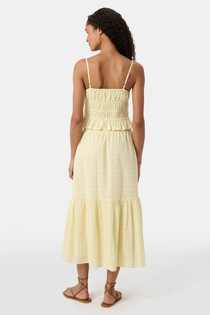 A person wears the Roller Rabbit Petal Eyelet Goldie Skirt, a butter yellow midi with eyelet details, ruffled hem, and gathered top, paired with strappy brown sandals. Their hands rest relaxed by their sides.