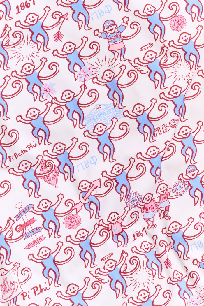 The Roller Rabbit Pi Beta Phi Monkey Polo Pajamas feature a short-sleeved button-up top and matching shorts, adorned with a playful pink and blue monkey print on a white background. Crafted from soft Pima cotton with an elastic waistband for comfort, these pajamas are made in Peru.