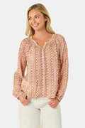 A woman stands smiling with one hand in her pocket against a plain white background, wearing the Roller Rabbit Priya Floral Colleen Top.
