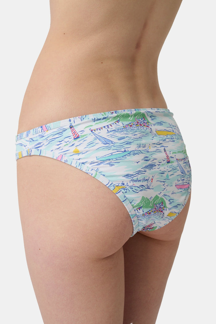 A person wears the Roller Rabbit Regatta Marais Bikini Bottom, featuring a colorful nautical print with boats and lighthouses. The UPF 50+ swimwear offers sun protection. Image is cropped from chest to upper thighs.