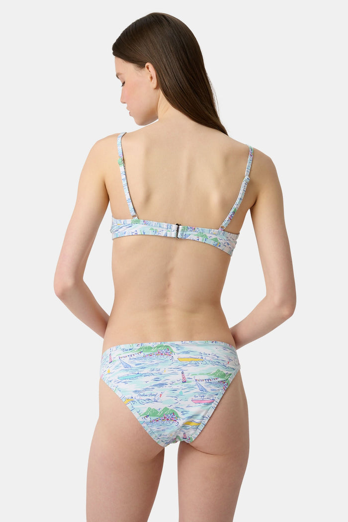 A person wears the Roller Rabbit Regatta Marais Bikini Bottom, featuring a colorful nautical print with boats and lighthouses. The UPF 50+ swimwear offers sun protection. Image is cropped from chest to upper thighs.