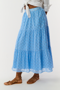 A person in a white, long-sleeved button-up shirt tied at the waist, the Roller Rabbit Ruban Carlisa Skirt, and brown strappy sandals stands against a white background.