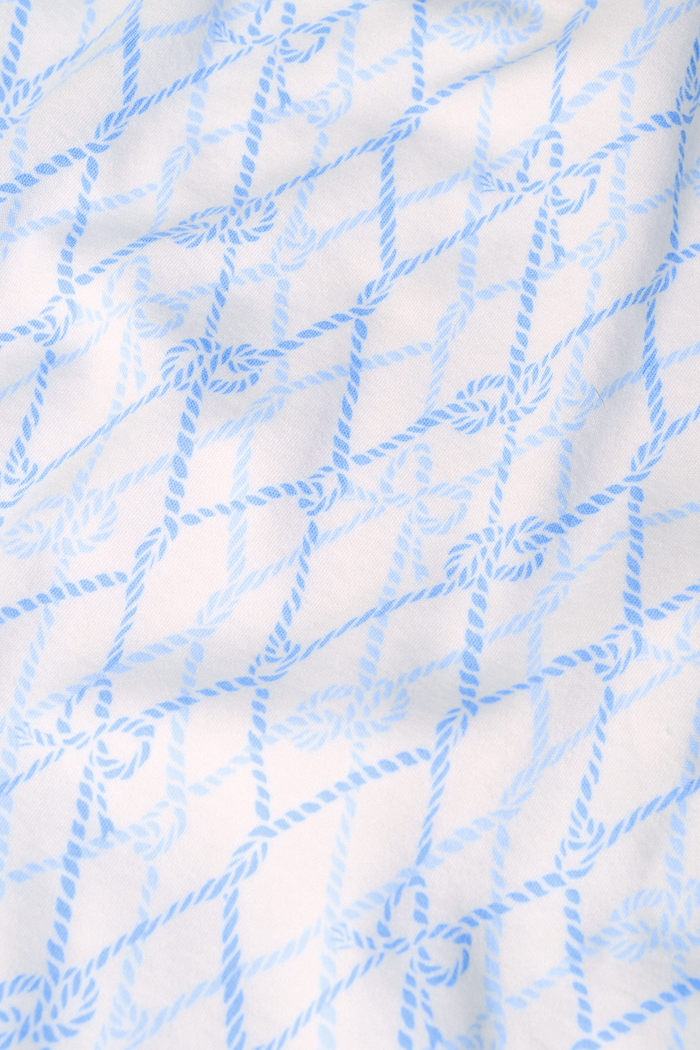 A woman with long curly hair smiles softly by a blue boat with striped canopy, wearing the Seaside Knots Ella Set by Roller Rabbit in a relaxed outdoor setting.