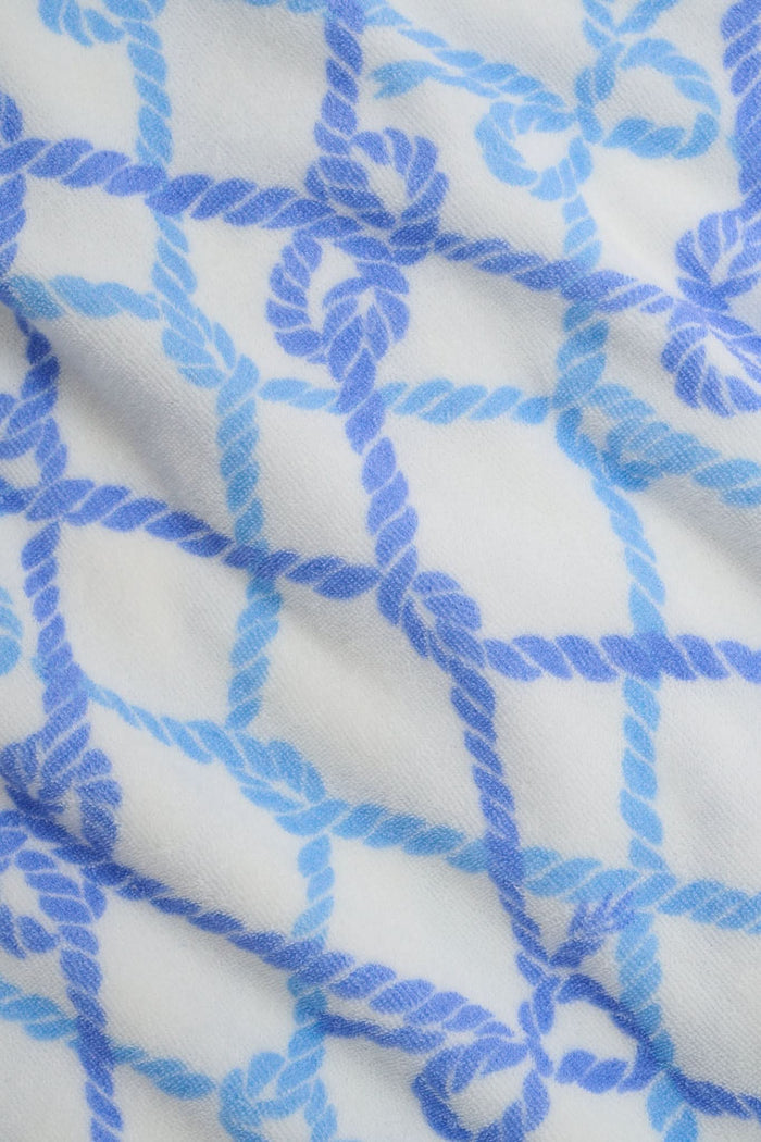 A person wears the Roller Rabbit Seaside Knots Mara Pant, featuring a tie waist and wide legs in loose white fabric with a light blue geometric chain pattern, paired with a matching top and white sandals against a plain white background.