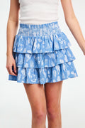 A person wears a white sleeveless top and a blue Seaside Stripe Siggy Skirt by Roller Rabbit, standing against a plain background.