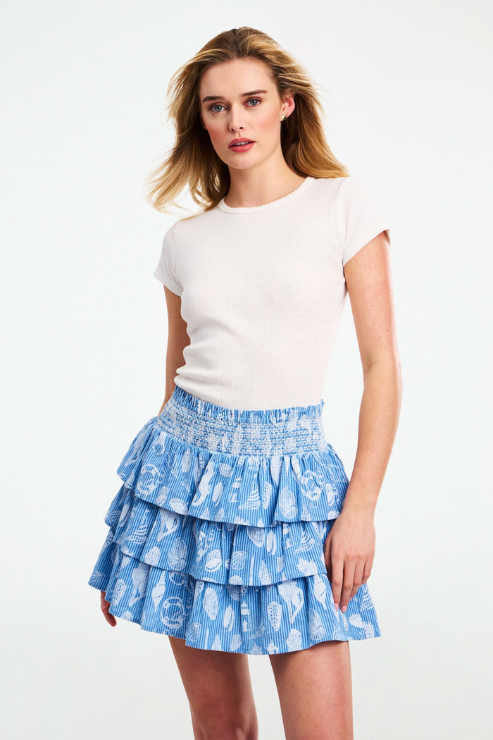 A person wears a white sleeveless top and a blue Seaside Stripe Siggy Skirt by Roller Rabbit, standing against a plain background.
