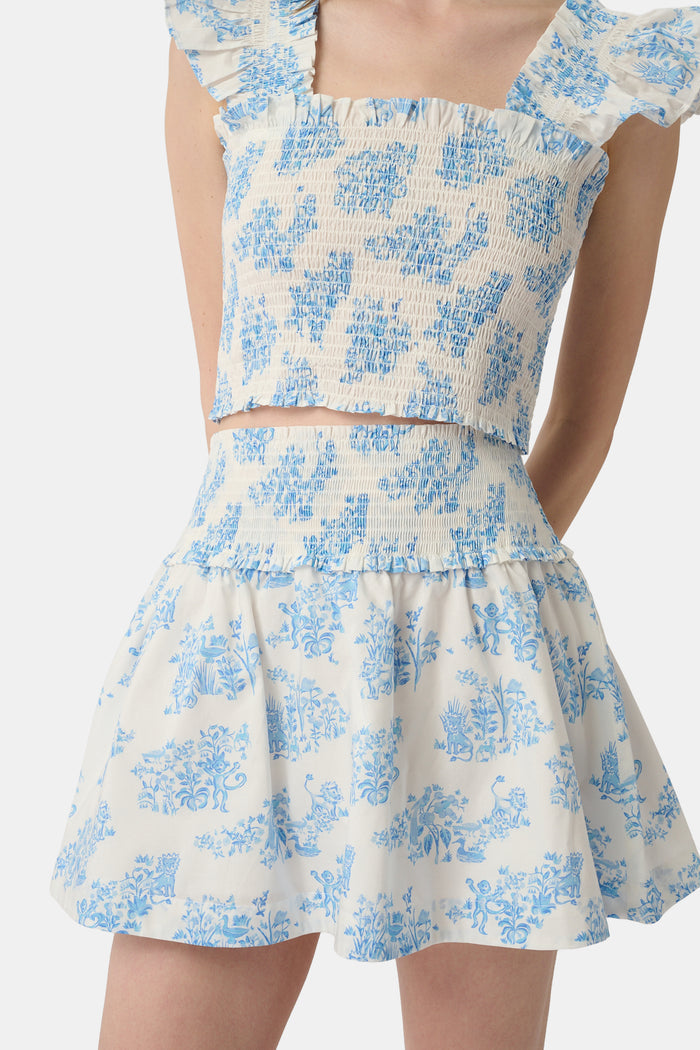A person wears a matching blue and white Sherwood Forest Monkey Delphine Mini Nap Skirt by Roller Rabbit and a ruffled crop top, standing against a plain background.