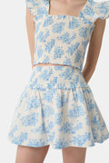 A person wears a matching blue and white Sherwood Forest Monkey Delphine Mini Nap Skirt by Roller Rabbit and a ruffled crop top, standing against a plain background.