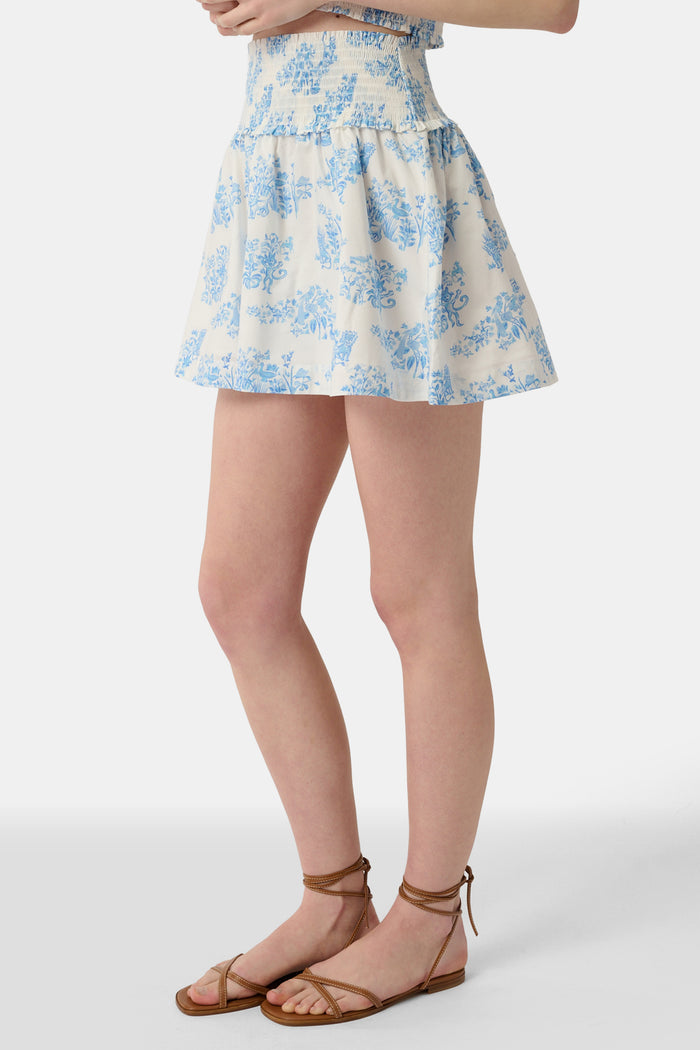 A person wears a matching blue and white Sherwood Forest Monkey Delphine Mini Nap Skirt by Roller Rabbit and a ruffled crop top, standing against a plain background.