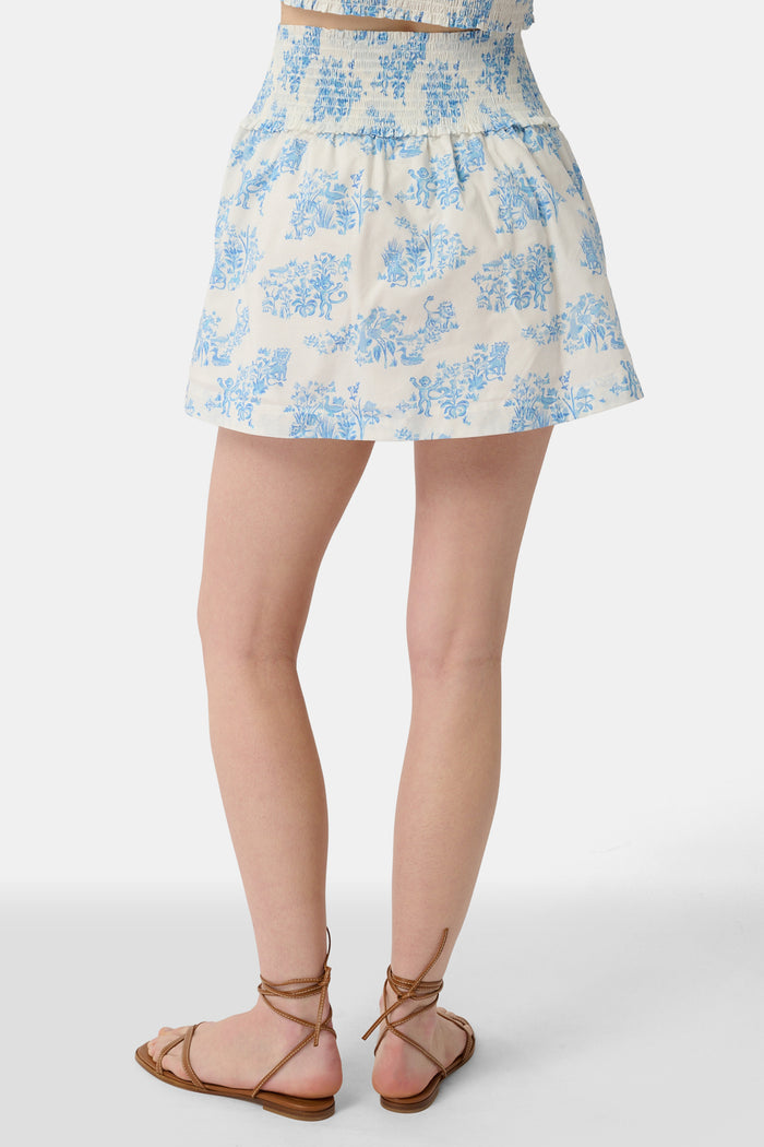 A person wears a matching blue and white Sherwood Forest Monkey Delphine Mini Nap Skirt by Roller Rabbit and a ruffled crop top, standing against a plain background.
