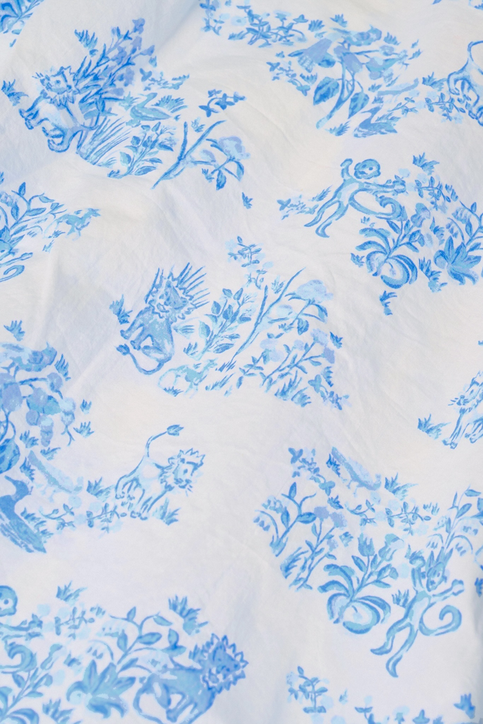 A person wears a matching blue and white Sherwood Forest Monkey Delphine Mini Nap Skirt by Roller Rabbit and a ruffled crop top, standing against a plain background.