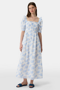 A woman wears the Roller Rabbit Sherwood Forest Monkey Scarlett Nap Dress—long, white with a blue monkey toile print, puffed short sleeves, smocked bodice, and square neckline—paired with blue slip-on sandals against a light background.