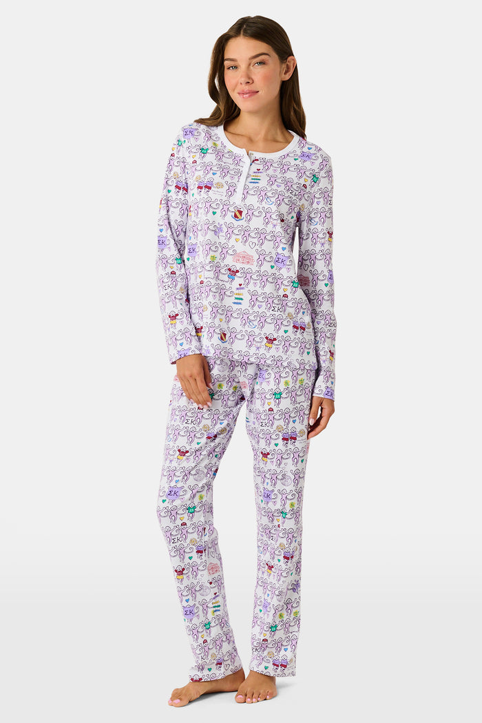 The Sigma Kappa Monkey Pajamas by Roller Rabbit is a long-sleeve set featuring a buttoned top and comfortable elastic waist, decorated with an all-over pattern of colorful cartoon monkey faces on a white background.
