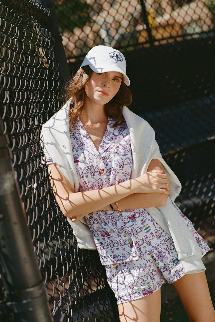 The Sigma Kappa Monkey Polo Pajamas by Roller Rabbit are a short-sleeve pajama set featuring matching shorts with a white background and colorful cartoon character pattern. Designed for comfort, they include a front button placket and an elastic waistband.
