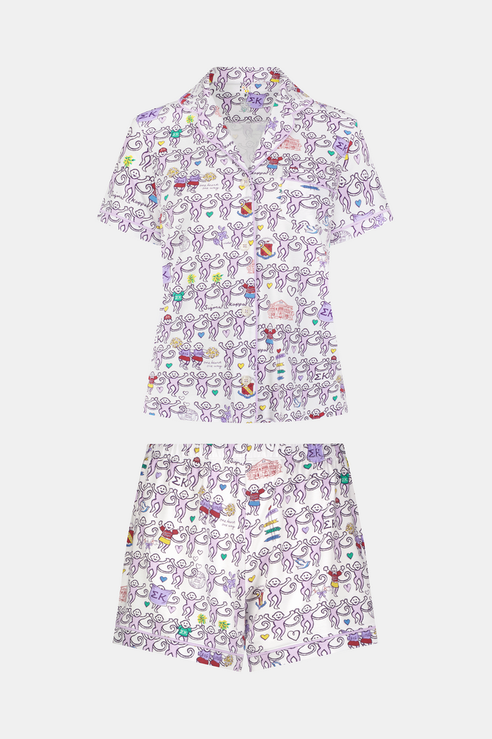 The Sigma Kappa Monkey Polo Pajamas by Roller Rabbit are a short-sleeve pajama set featuring matching shorts with a white background and colorful cartoon character pattern. Designed for comfort, they include a front button placket and an elastic waistband.