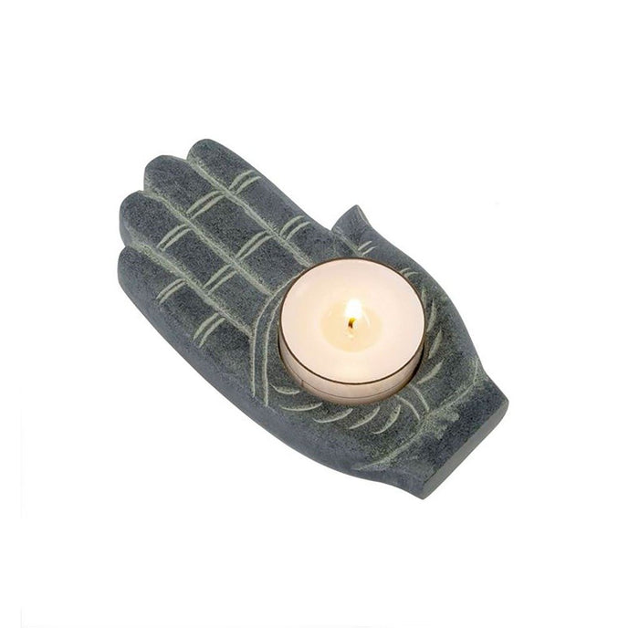 A gray soapstone hand-shaped candle holder with a lit candle inside.