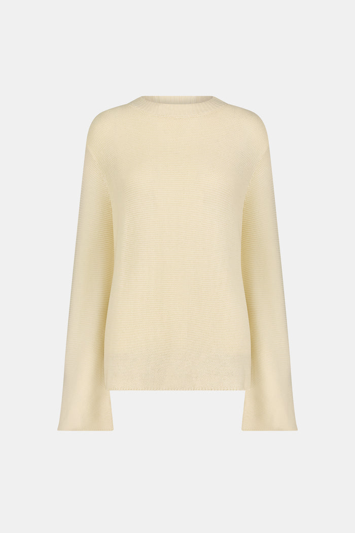 A woman wearing the Roller Rabbit Soleil Sweater, a cream cashmere blend pullover with wide sleeves, paired with patterned blue and white pants, stands against a plain white background.