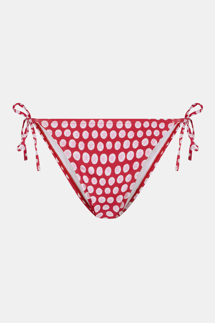 A person wears the Roller Rabbit Starry Dot Isa Bikini Bottom in red with white polka dots and adjustable hip ties, shown from mid-torso to upper thigh.
