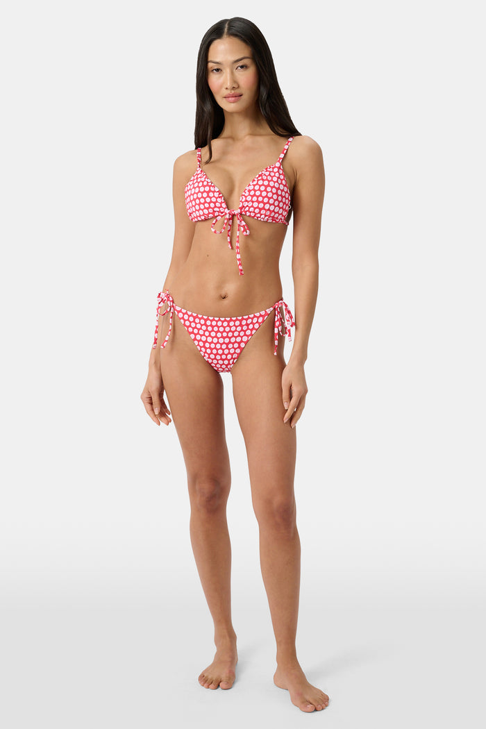 A person wears the Roller Rabbit Starry Dot Isa Bikini Bottom in red with white polka dots and adjustable hip ties, shown from mid-torso to upper thigh.