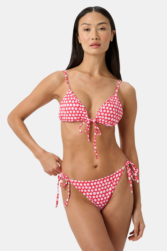 A woman wears the Roller Rabbit Starry Dot Isa Bikini Top, a red triangle bikini with white polka dots and a front tie, shown from shoulders to waist against a plain background.